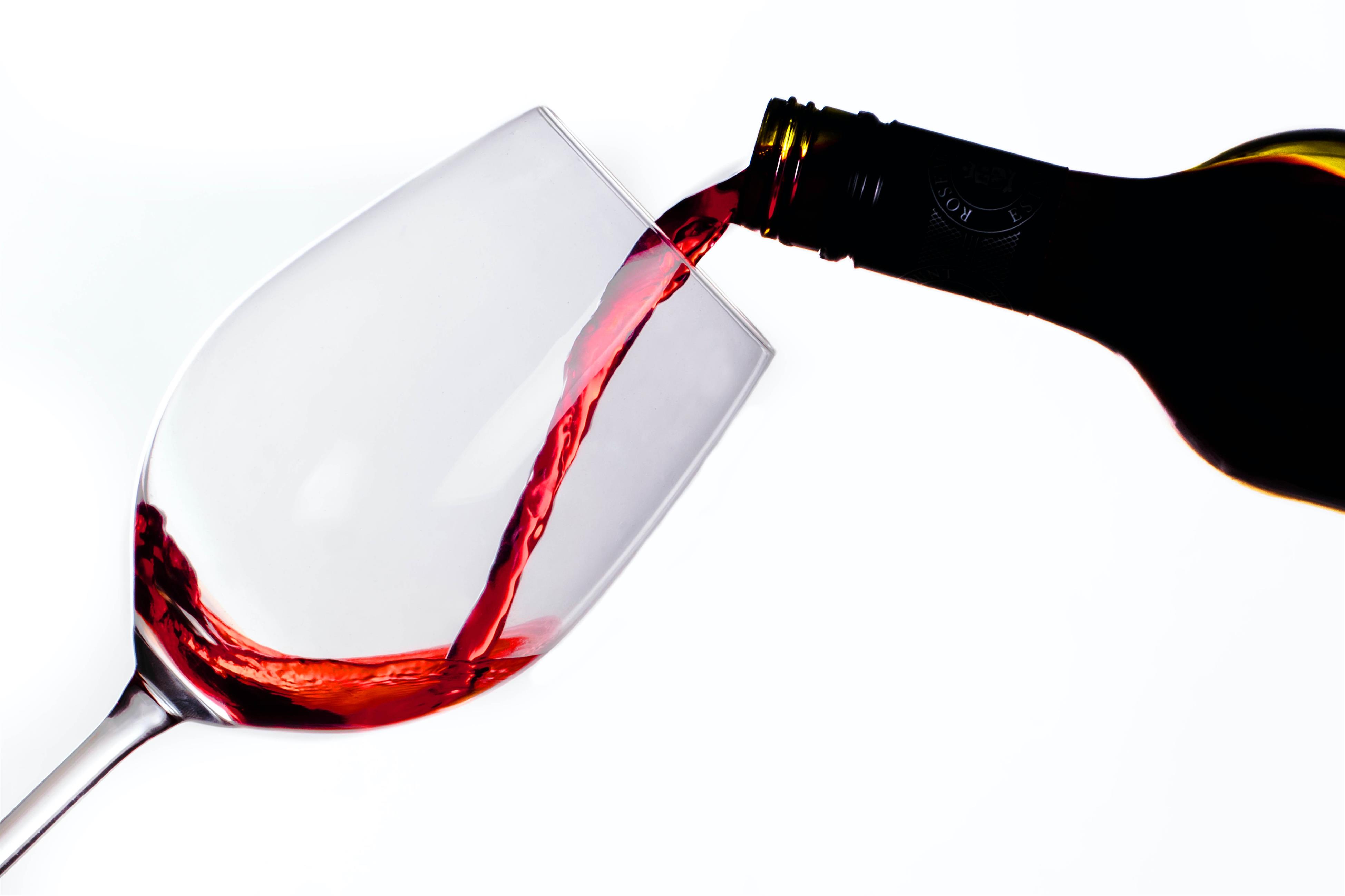 Rotwein wird aus Flasche in ein Rotweinglas gefüllt