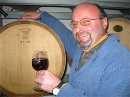 Lachender Mensch mit Weinglas in der Hand vor Weinfass stehend